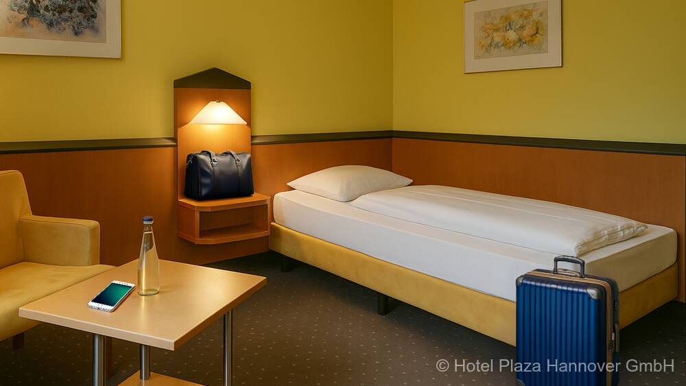 Einzelzimmer mit gemütlichen Bett und einer Sitzecke. Der Raum ist mit Holzmöbeln und in warmen Farben ausgestattet.