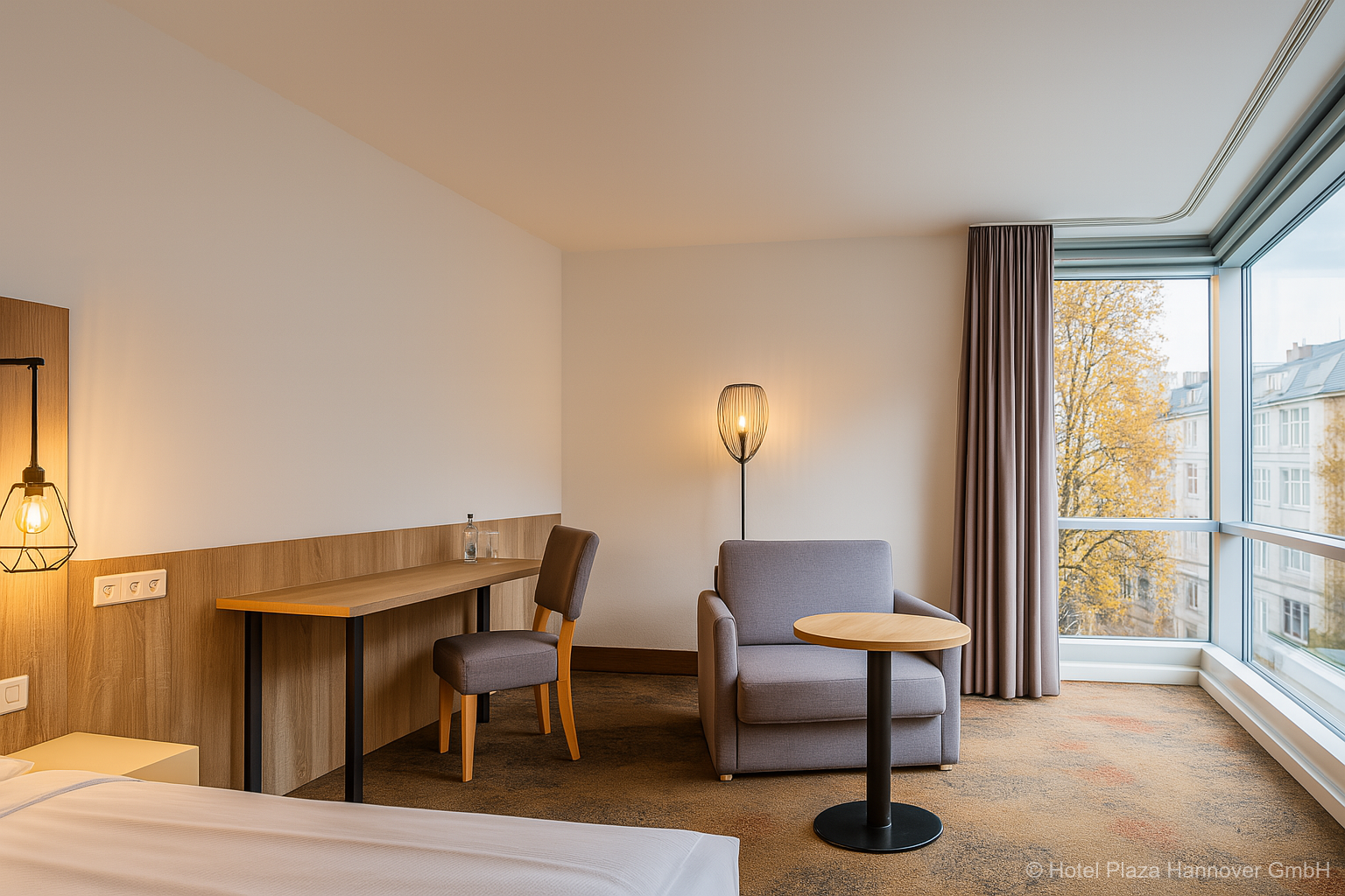 Geräumiges, modernes Hotelzimmer mit bodentiefen Fenstern, einem großzügigen Schreibtisch und einem einladenden Sessel am Fenster.