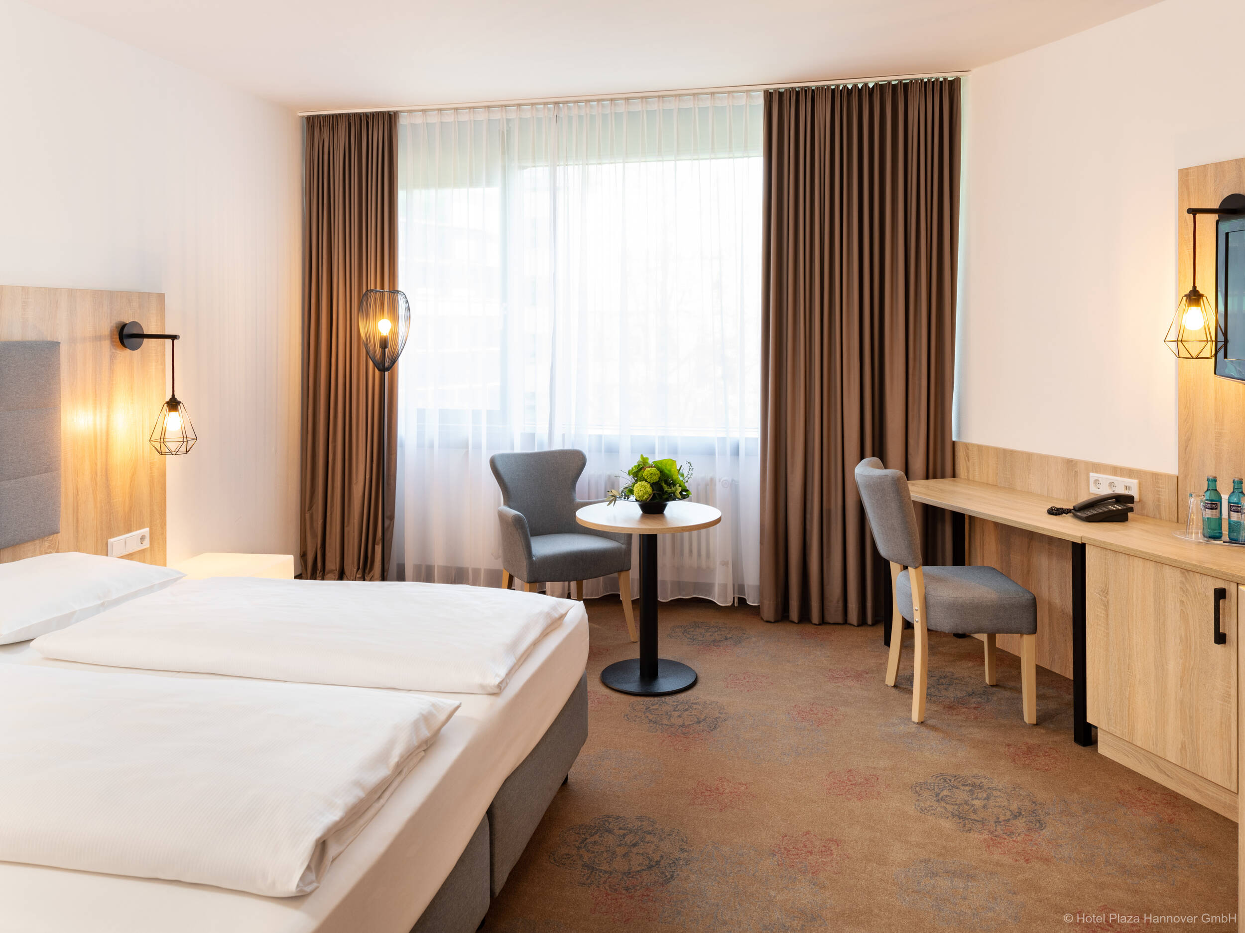 Modern eingerichtetes Hotelzimmer mit Queensizebett, Sitzecke am Fenster und großzügigem Schreibtisch mit Flachbild-TV.