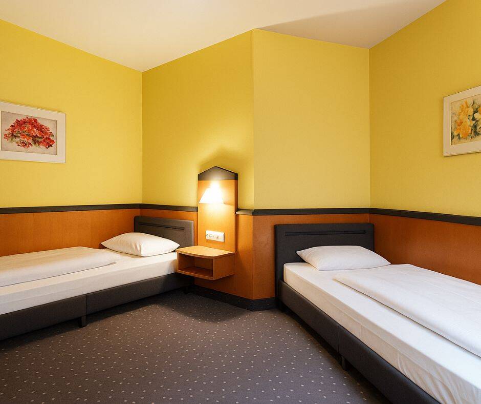 Zwei Einzelbetten stehen über Eck in einem in warmen Farben gestrichenen Hotelzimmer